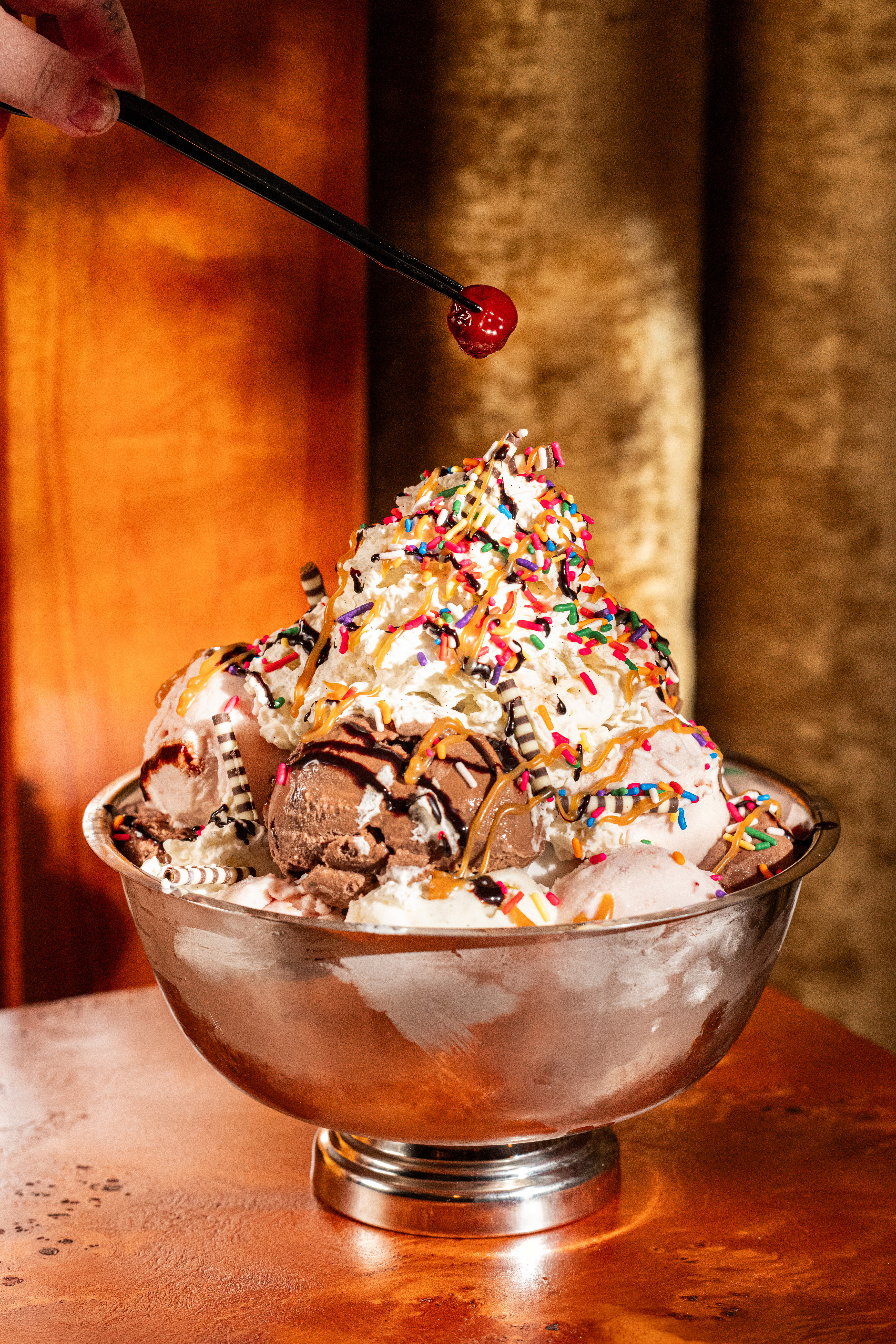 Delilah's decadent ice cream sundae topped with whipped cream, chocolate, caramel drizzle, rainbow sprinkles, and a cherry