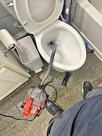 Plumber clearing a clogged toilet with a drain auger in a Rockwall bathroom