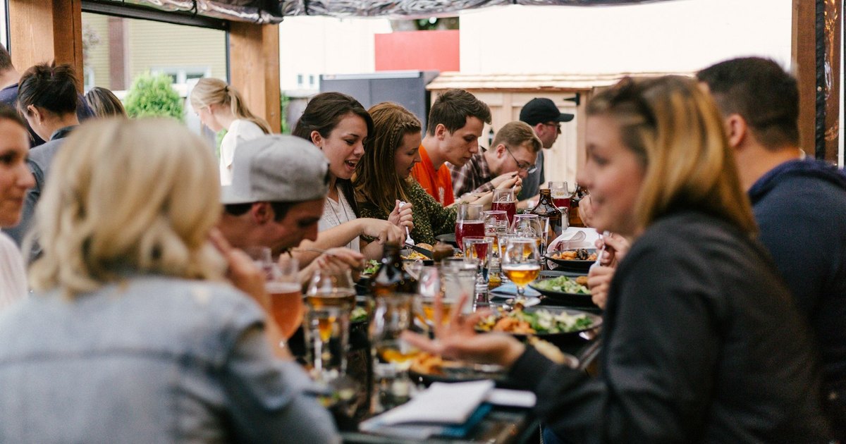 Group of neighbors sharing lunch and drinks at a long table on a restaurant patio